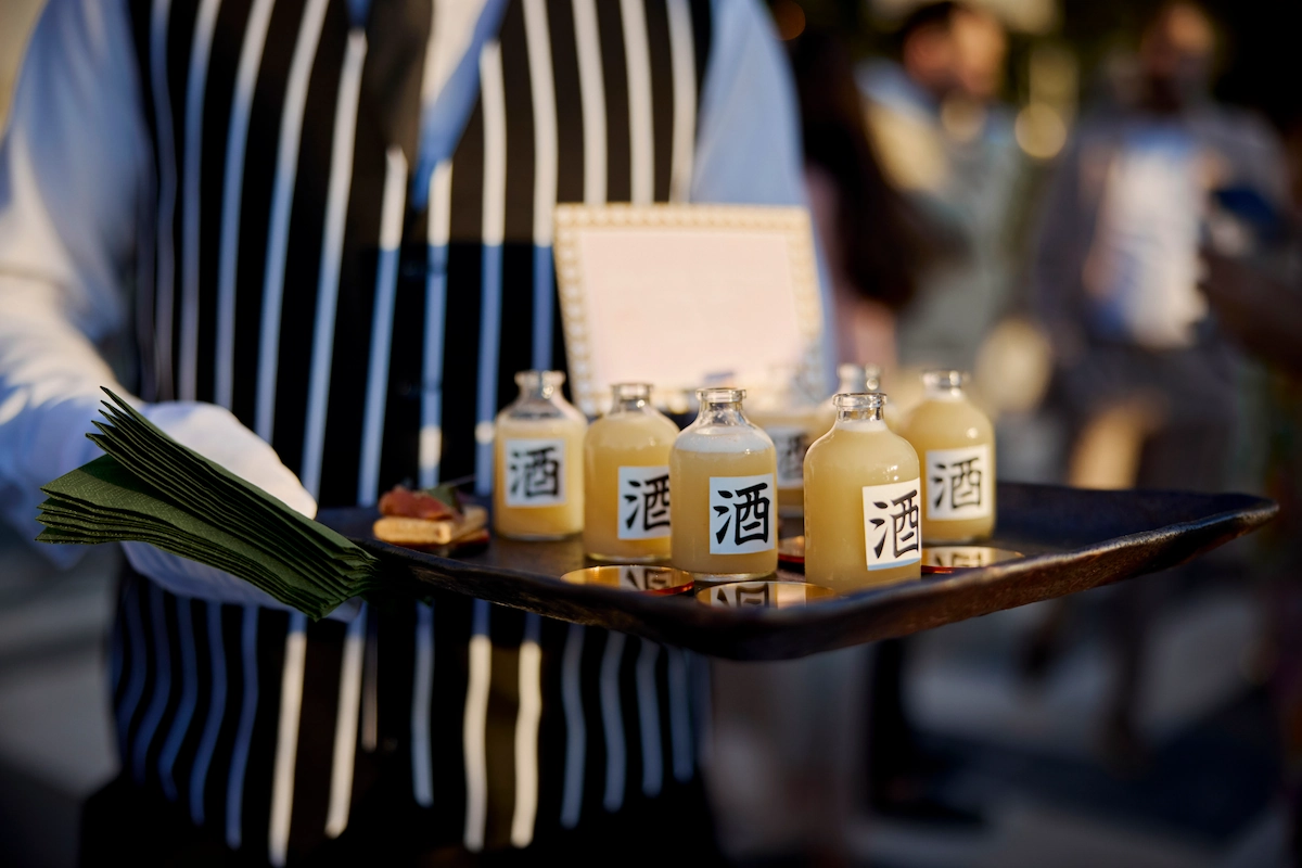 A waiter carrying a tray of small sake bottles and canapés at an evening reception