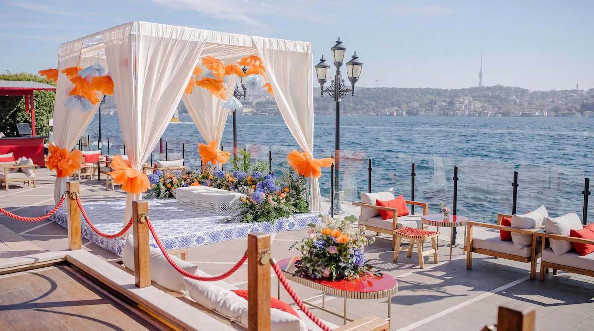A wedding mandap dressed with orange and blue flowers on a waterfront terrace by the sea