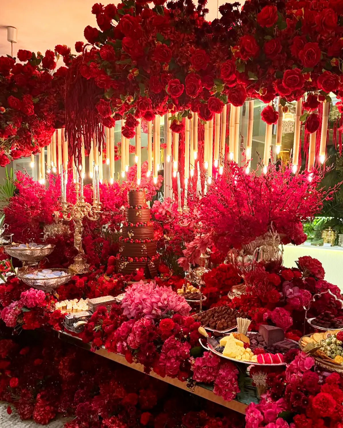 Tall taper candles rising above a dramatic red floral table display