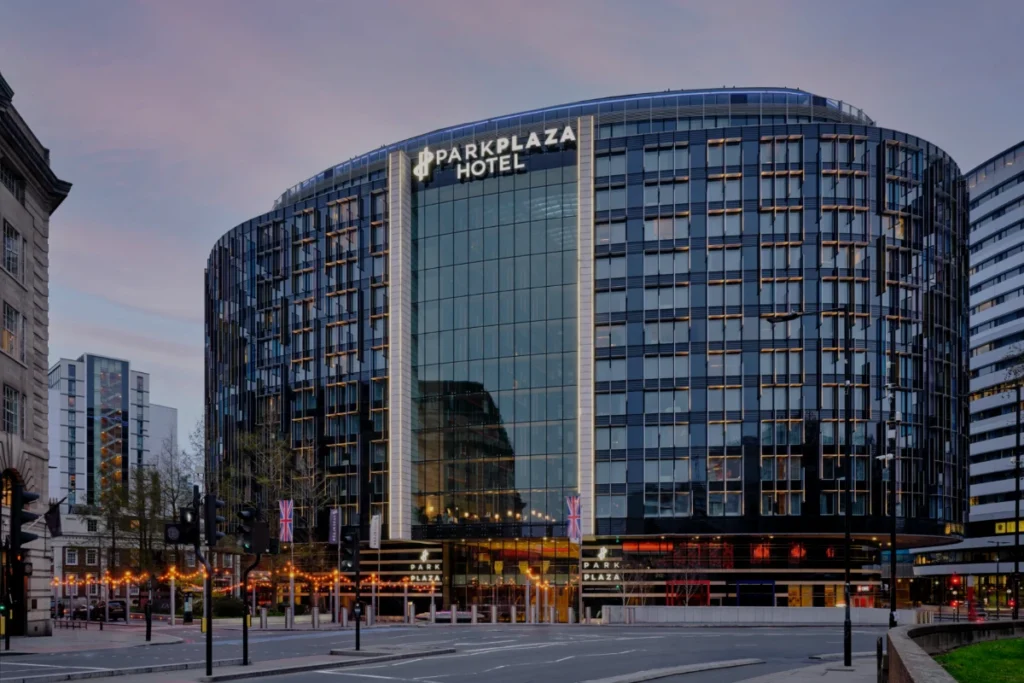 Park Plaza London Westminster Bridge at dusk – a curved glass façade lit from within, with Union flags and festoon lights along the street outside